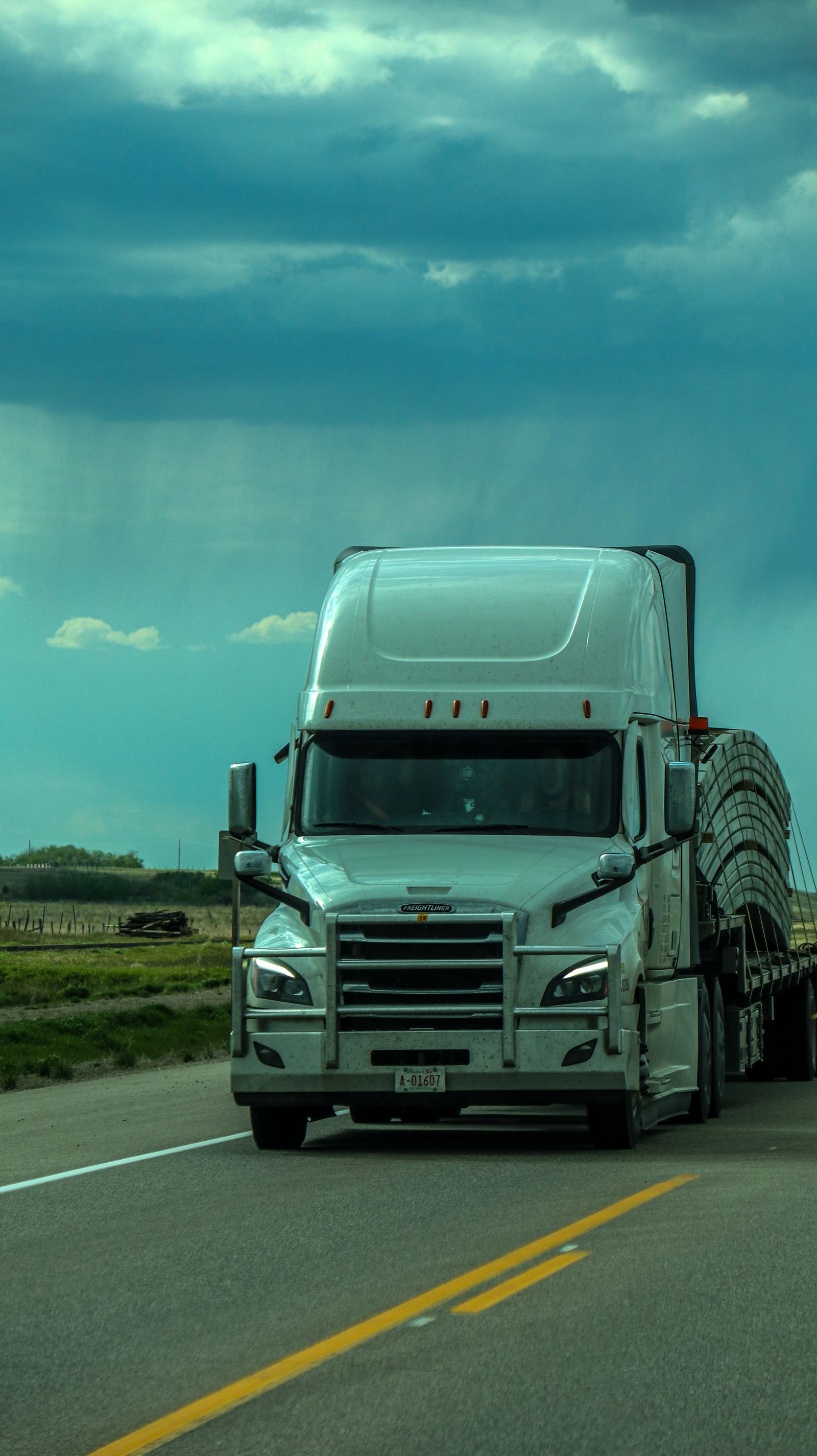 White Freightliner Cascadia hauling under a stormy sky